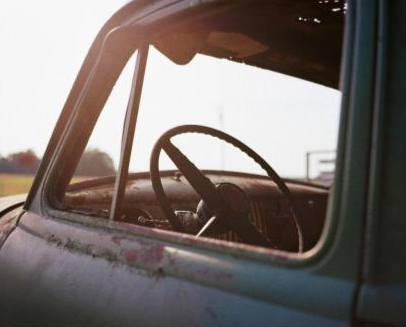 The interior of an abandoned car with the driver's side window broken.