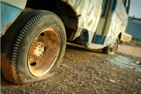 A flat tire on a rusted and abandoned bus.