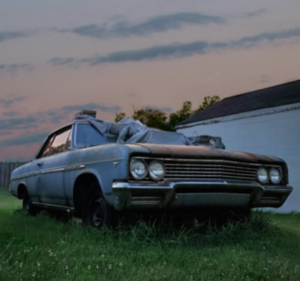 An old, rusty car abandoned in a grassy area.