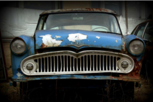  An old, rusty blue car with a chipped windshield and a damaged grille.