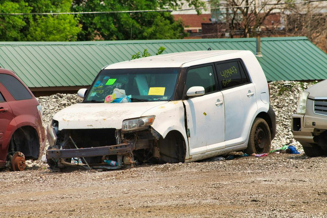 A damaged white car with a missing front bumper and other visible damage.