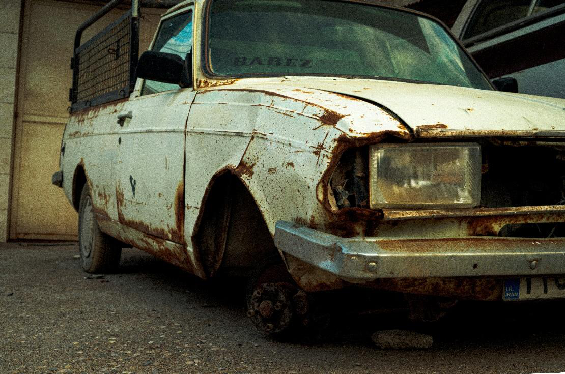 A rusty and abandoned junk car with flat tires and missing parts parked outside.