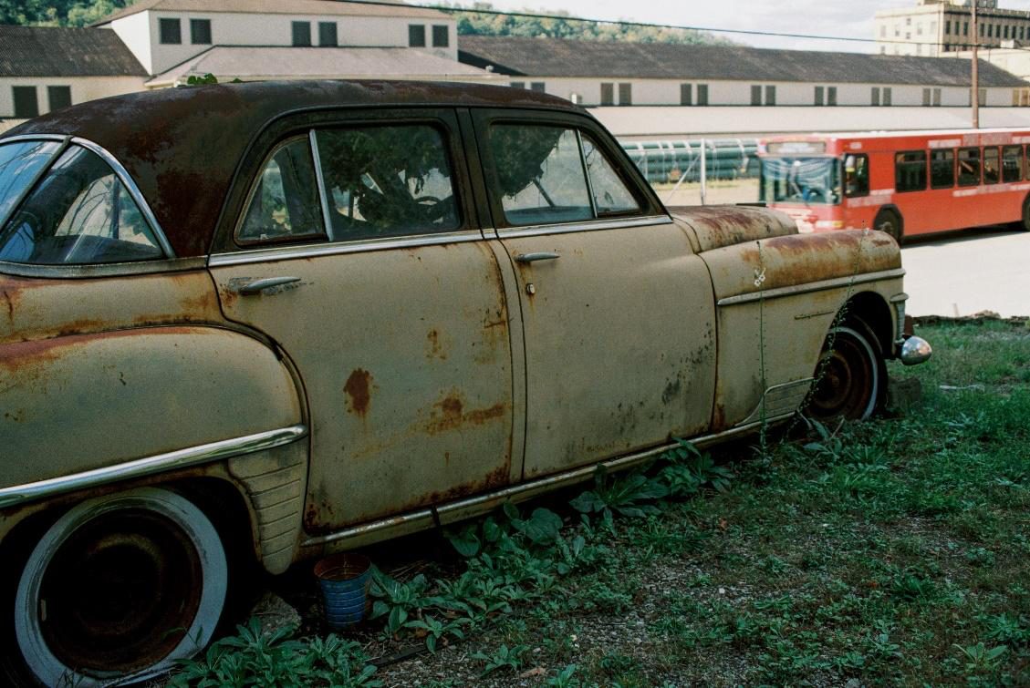 A faded, old junk car with flat tires and visible rust parked outside.