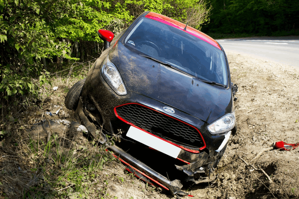 Damaged black and red Ford car stuck in a ditch after an accident near a roadside.
