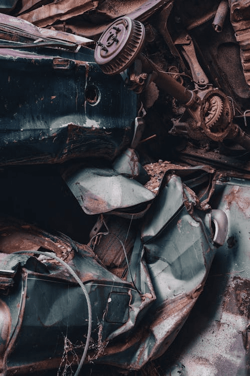 Close-up of a crushed green car with rust and visible metal damage.