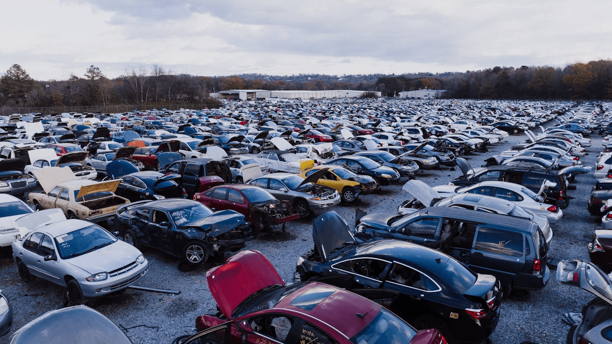 A vast junkyard filled with rows of damaged and salvaged cars under a cloudy sky.